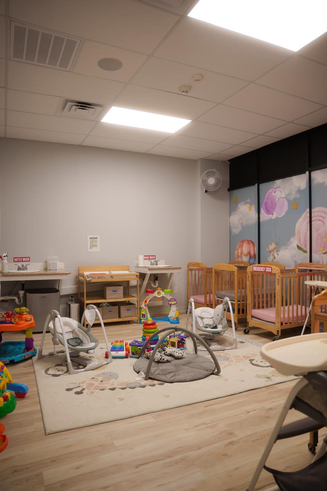 Clean infant room with cribs, activity equipment and care stations
